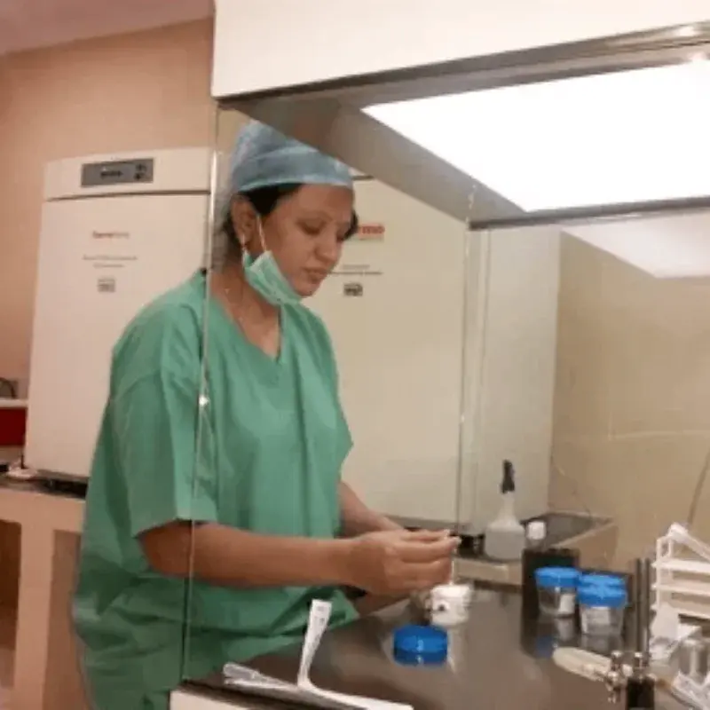 An embryologist in green scrubs working at the laminar flow hood in the centre’s embryology laboratory, beside an incubator