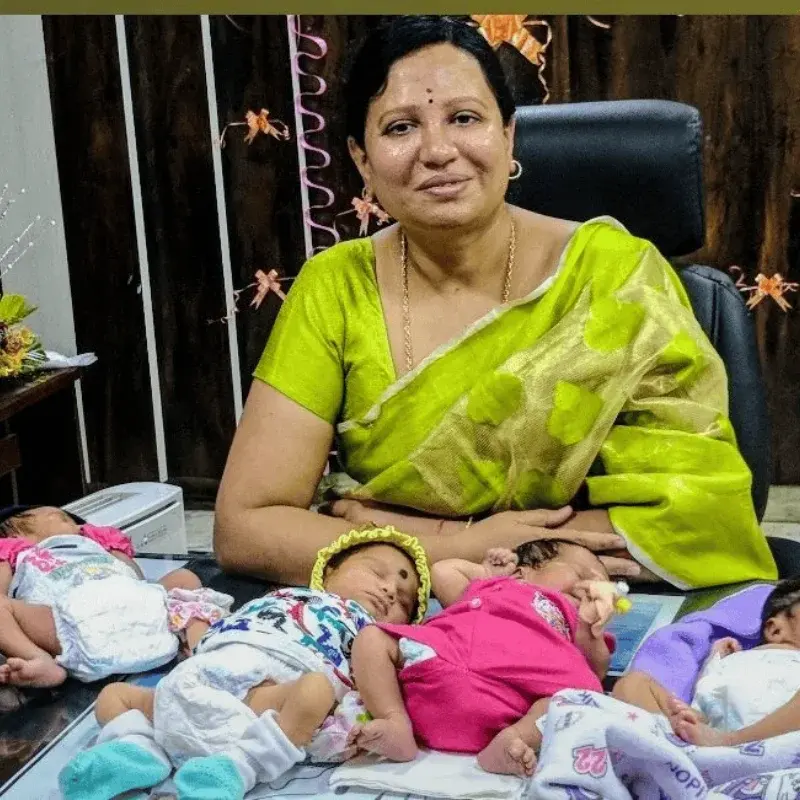 Dr. Padmaja in a green sari at her desk with five babies born at the centre laid out in front of her