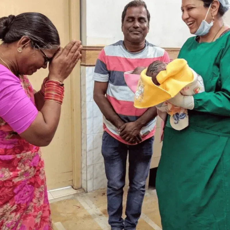 A grandmother with her hands folded in thanks and a father looking on as a member of the team presents their newborn