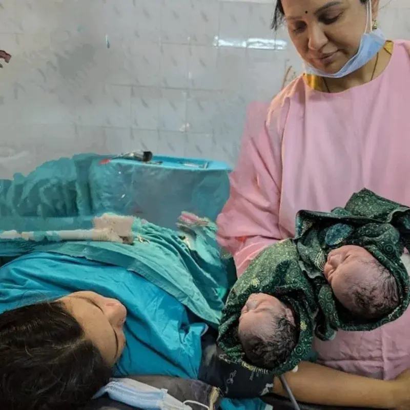 A member of the team holding newborn twins in a green wrap beside their mother shortly after delivery