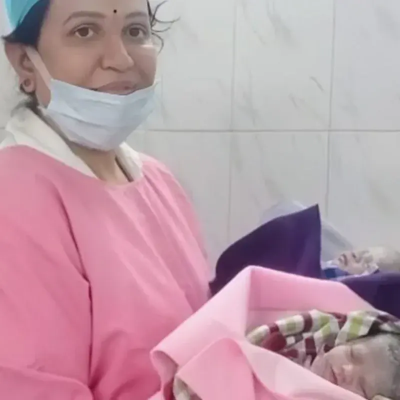 A member of the care team holding a newborn in a pink blanket, with a second baby resting alongside
